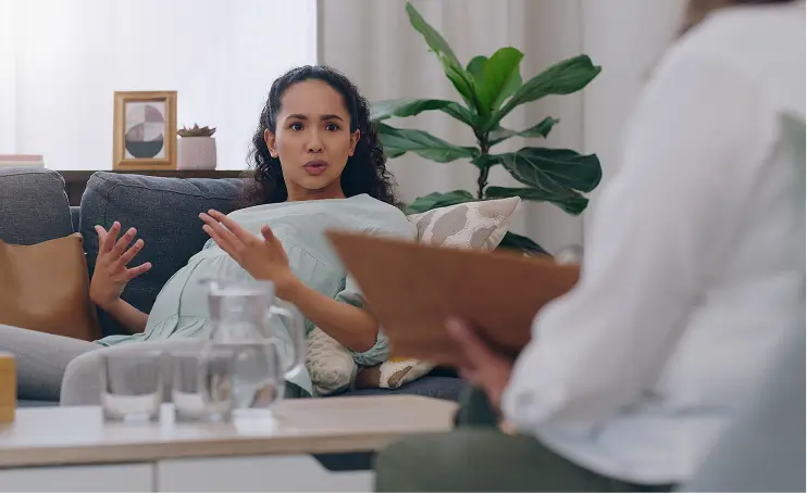A pregnant woman talks expressively to a therapist during a session